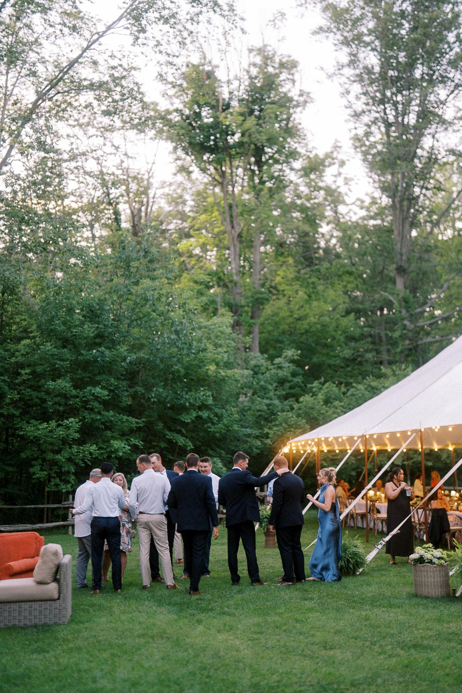 Wedding guests gather on a lawn beside a white reception tent with string lights at a private farm estate near Chatham-Kent, Ontario, Canada.
