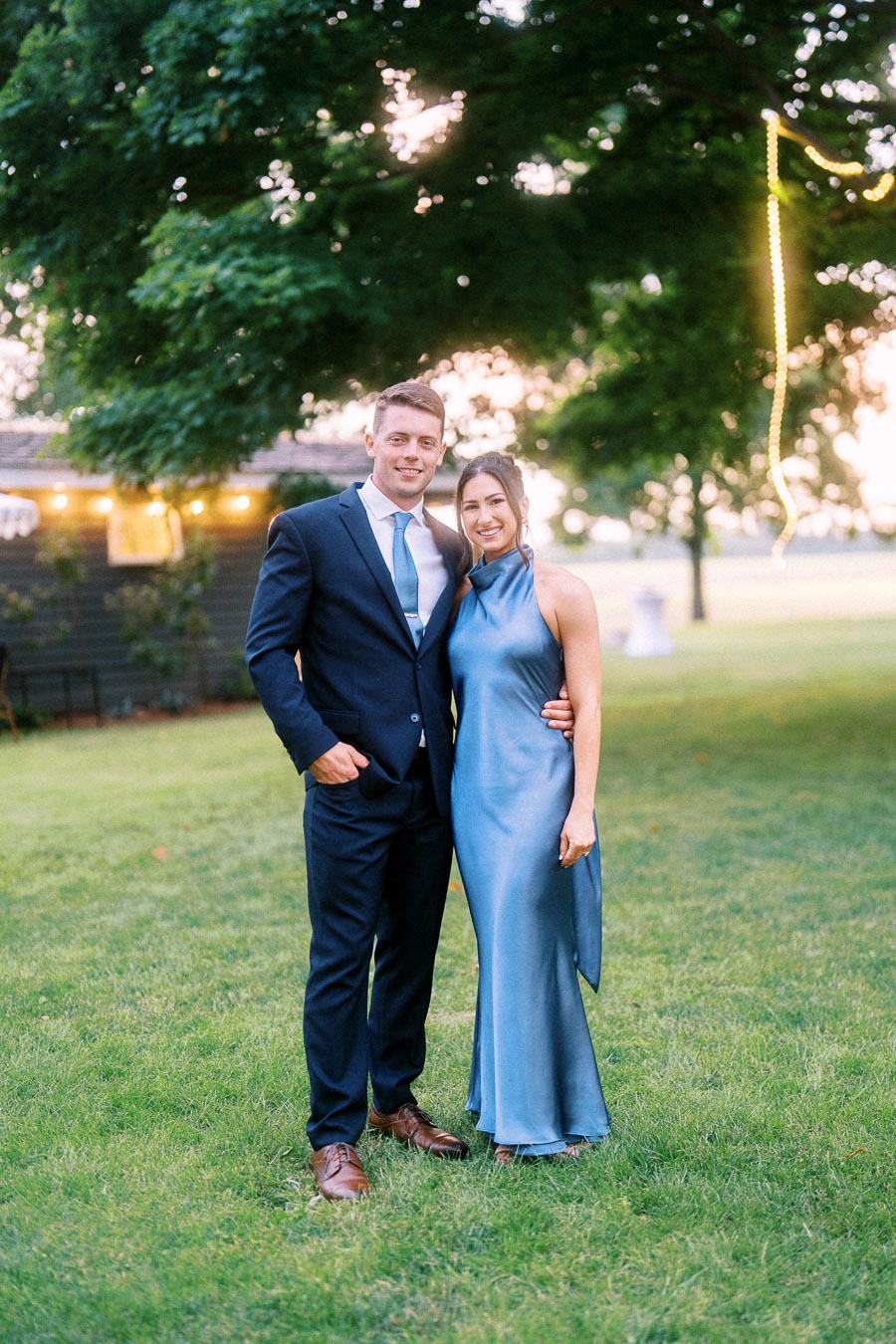 Wedding guests posing on a grassy private estate lawn near Chatham-Kent, Ontario, with trees and warm string lights at sunset.