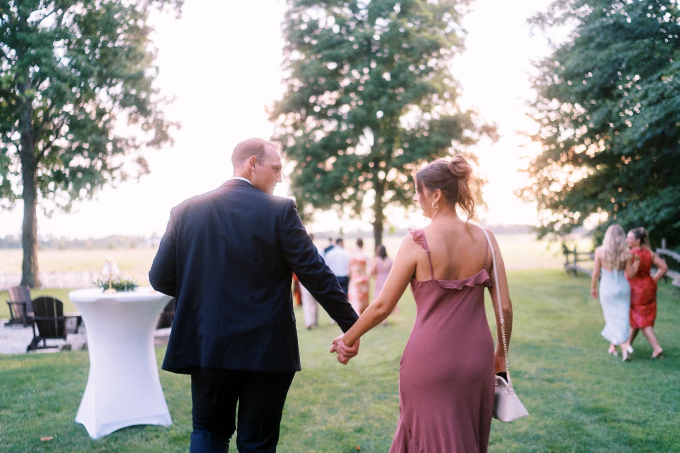 Wedding guests holding hands while walking across a lawn at a private estate outdoor farm wedding near Chatham-Kent, Ontario, Canada.