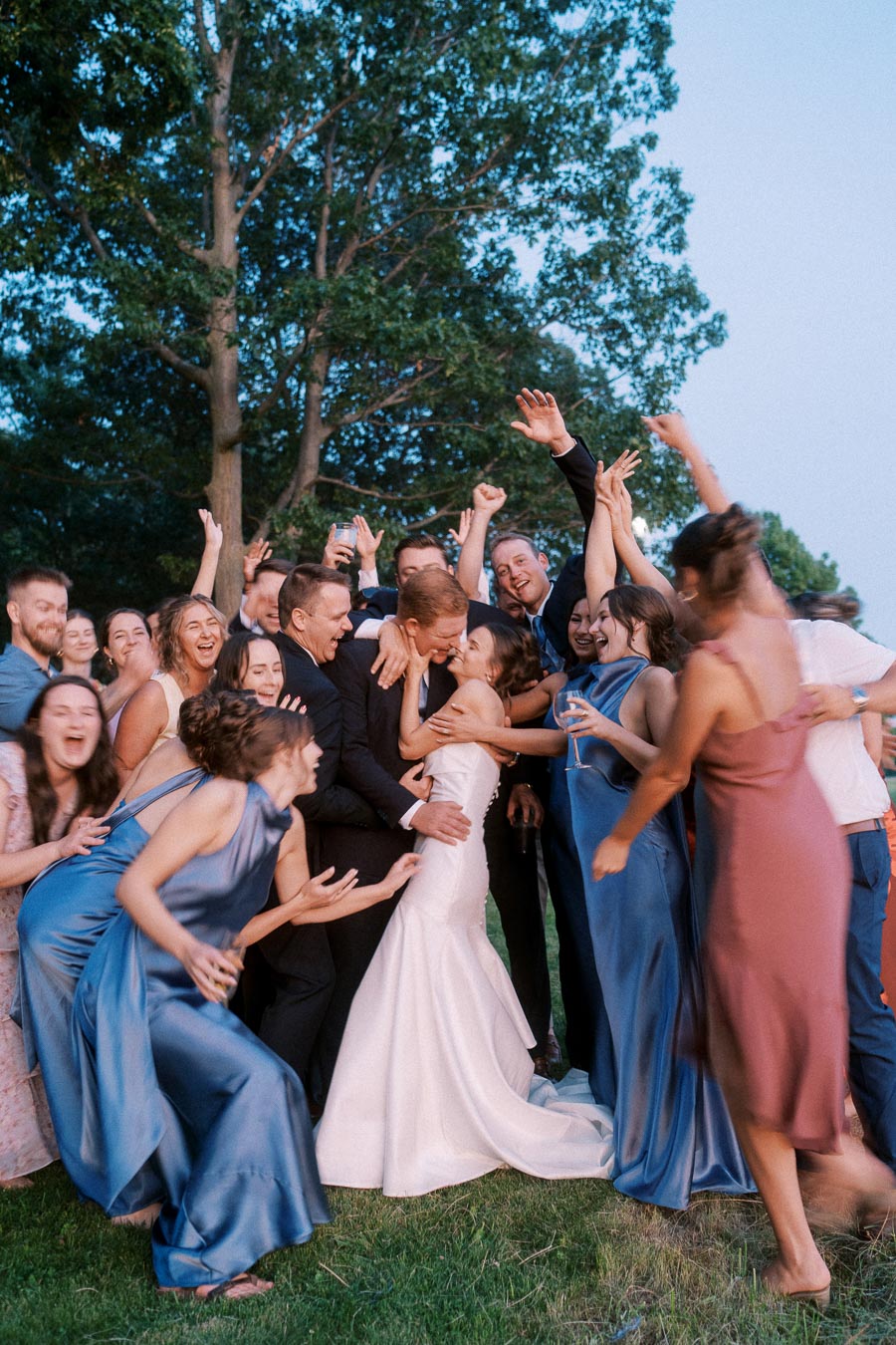 Bride and groom kissing as wedding party cheers around them at an outdoor farm wedding near Chatham-Kent, Ontario, Canada.