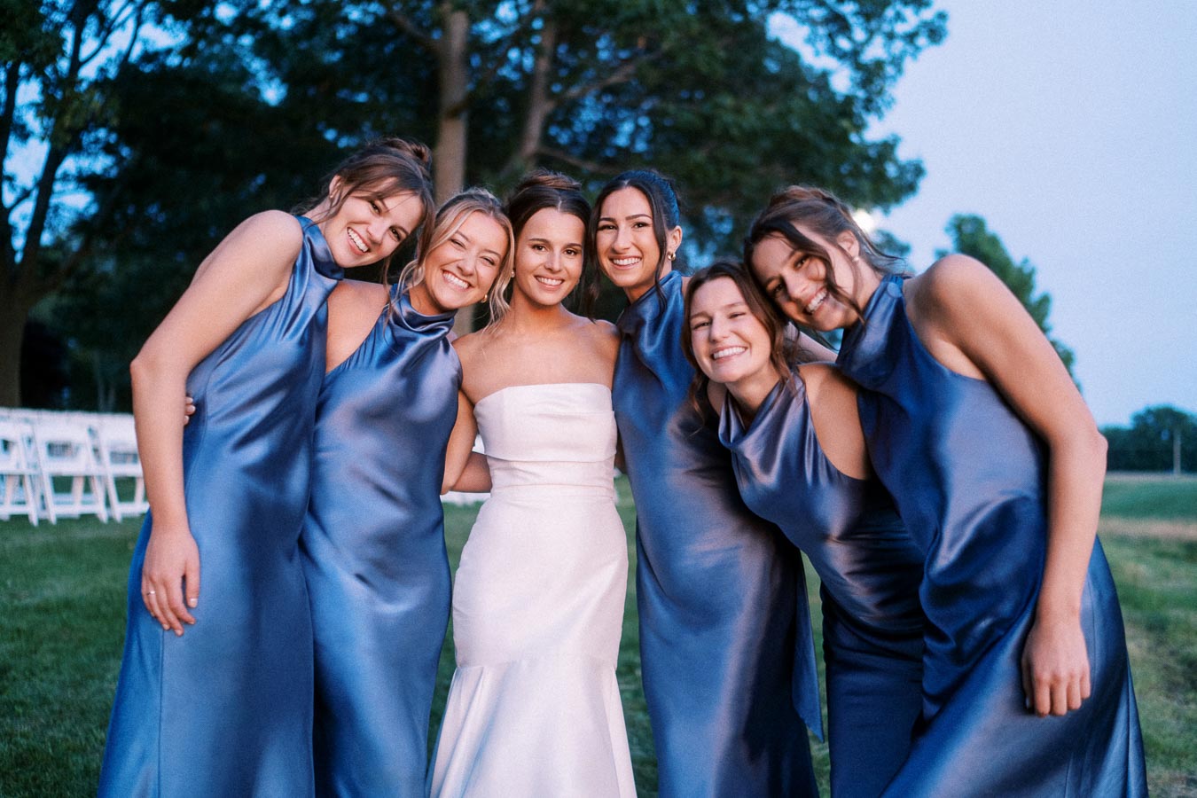 Bride in white gown posing outdoors with five bridesmaids in blue satin dresses at a private estate farm wedding near Chatham-Kent, Ontario.
