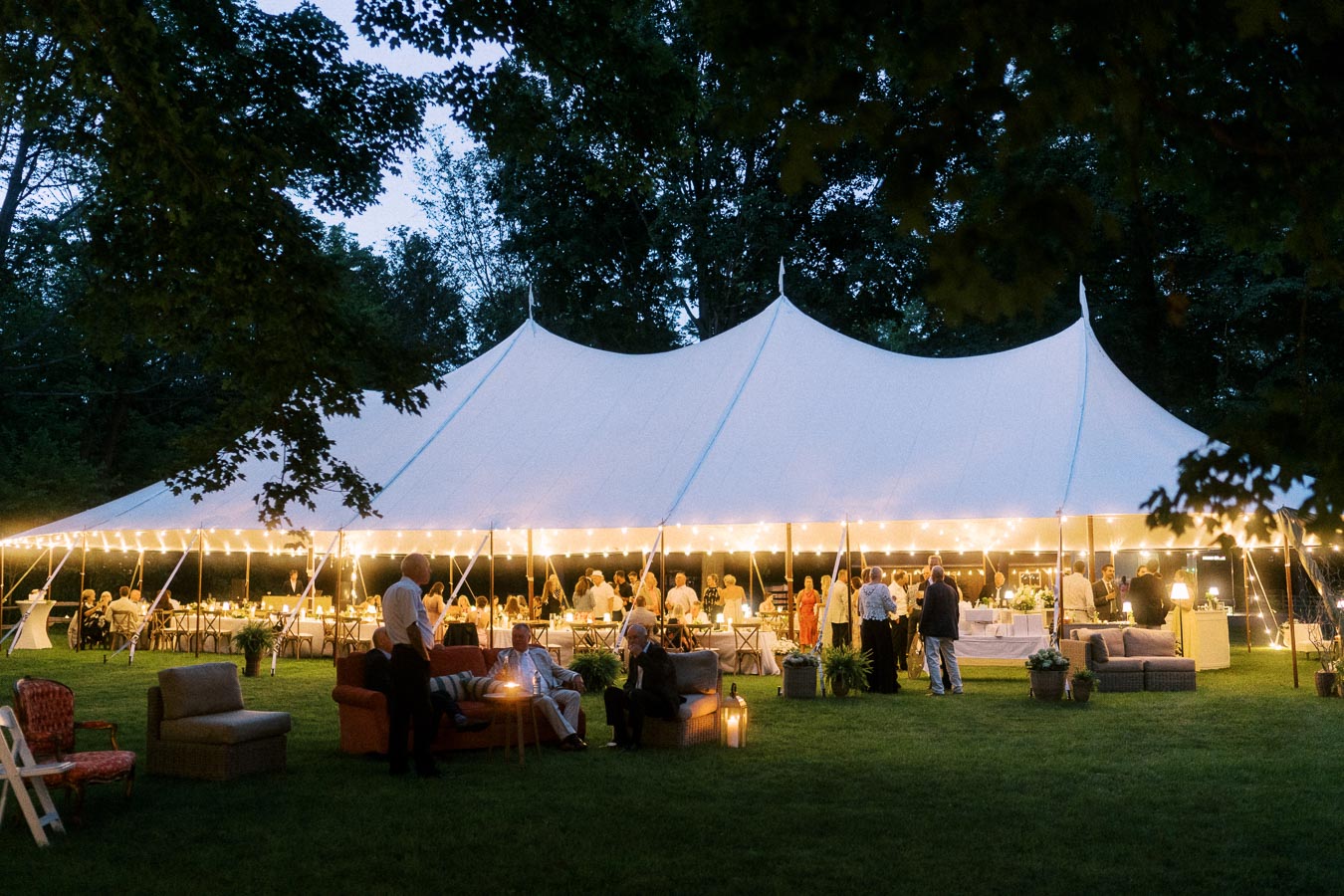 Outdoor tented wedding reception at dusk on a private farm estate near Chatham-Kent, Ontario, with guests dining under a white marquee and string lights.