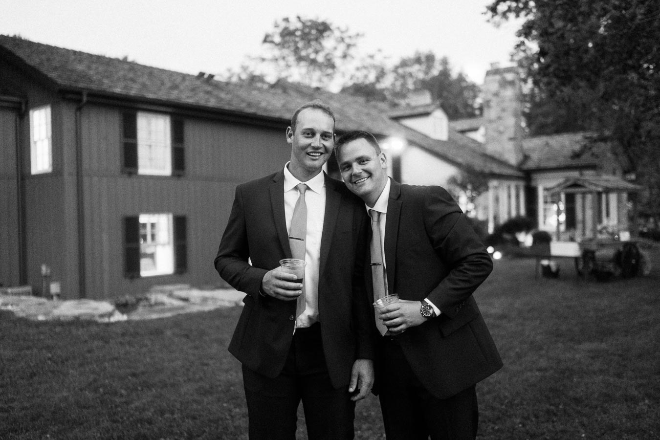 Two men in suits smiling with drinks at a private estate outdoor wedding near Chatham-Kent, Ontario.