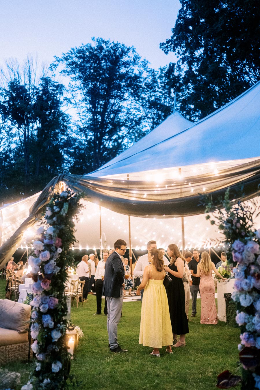 Guests gather outside a glowing tented wedding reception on a private estate near Chatham-Kent, Ontario, with floral arches and string lights at dusk.