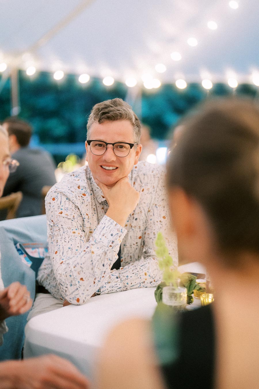 Man with glasses smiling at a table during an outdoor tented wedding dinner near Chatham-Kent, Ontario, Canada.