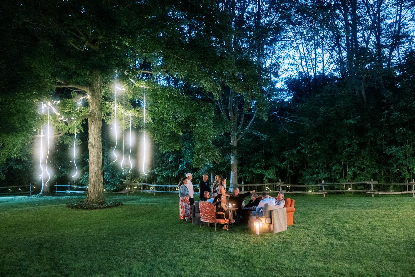 Outdoor wedding guests gather on lawn seating at dusk under glowing tree lights on a private farm estate near Chatham-Kent, Ontario, Canada.