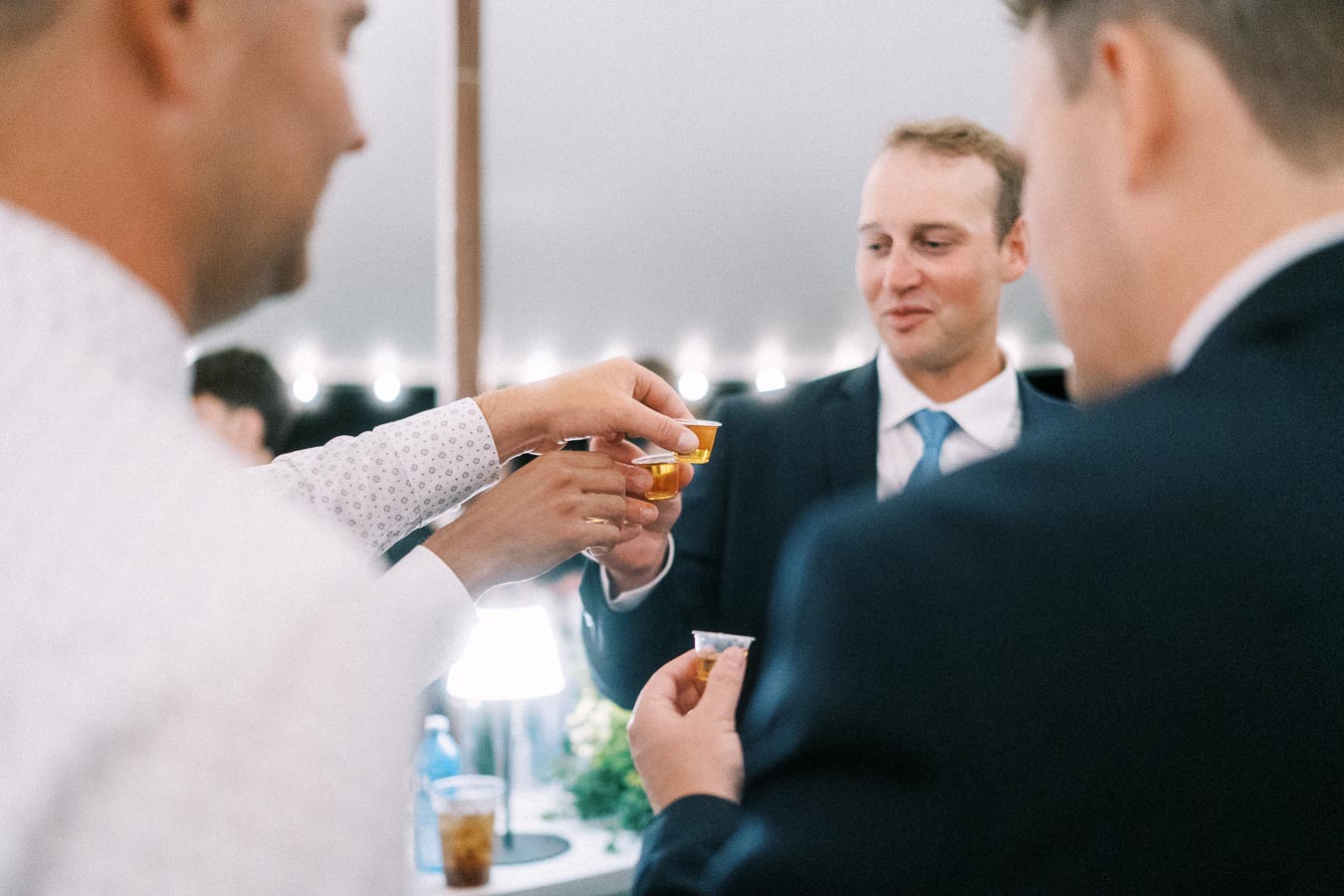 Men in suits raise small plastic cups for a toast during a tented wedding reception on a private estate near Chatham-Kent, Ontario.
