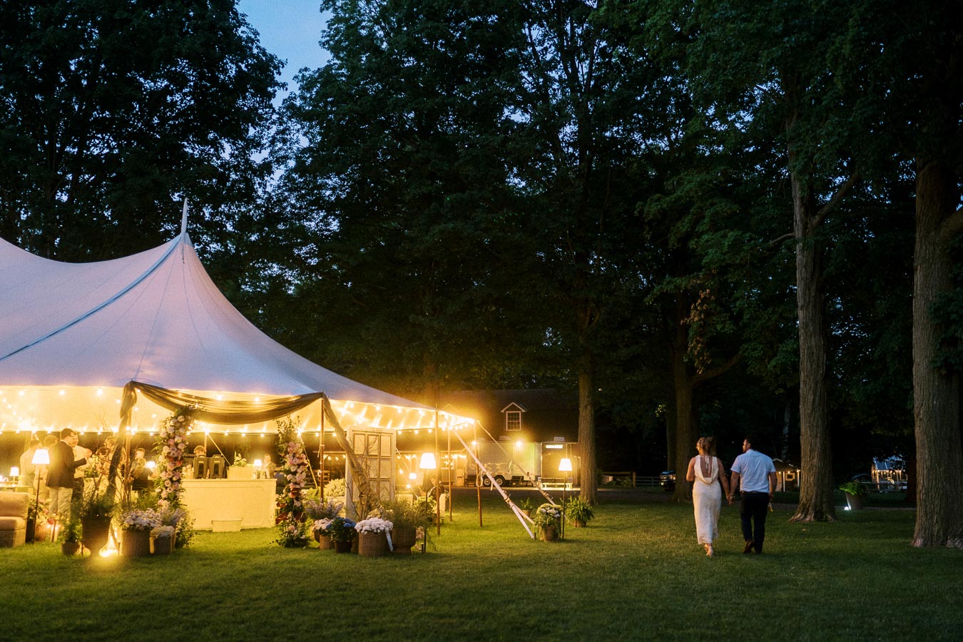 Bride and groom walking on a lawn beside a glowing white wedding tent at a private estate near Chatham-Kent, Ontario, Canada.