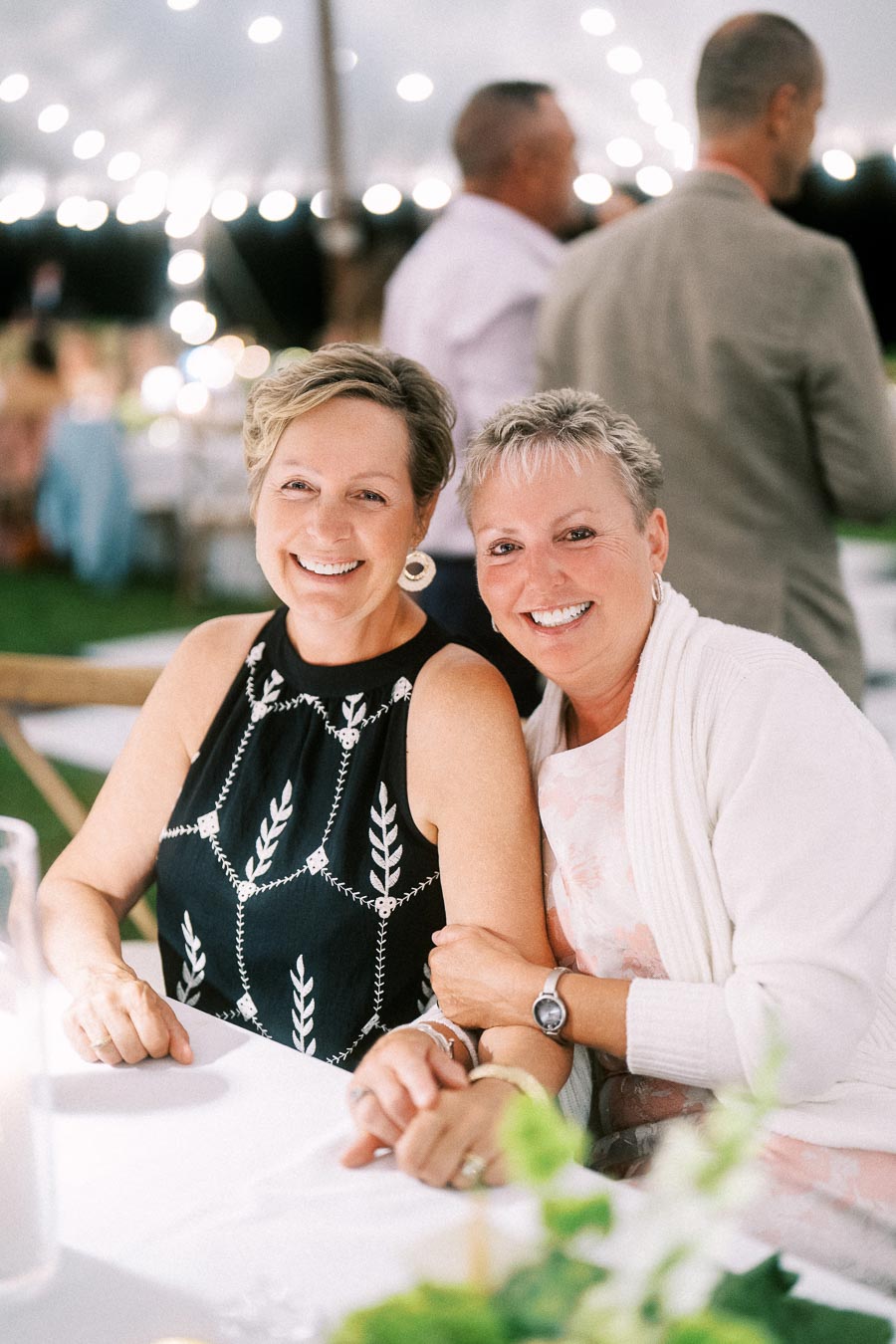 Two smiling women seated together at a tented outdoor farm wedding dinner near Chatham-Kent, Ontario.
