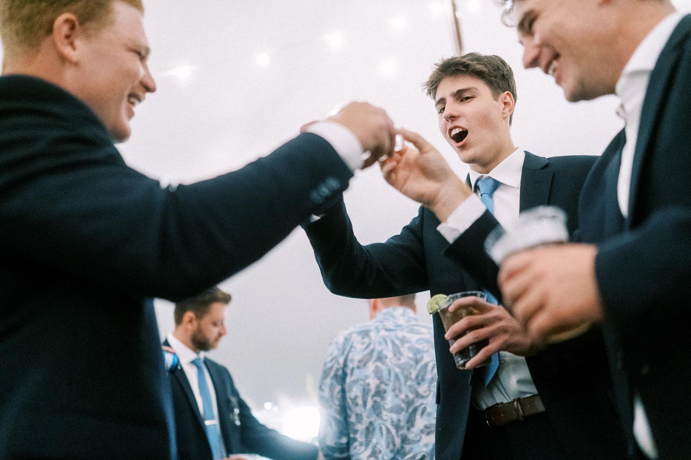 Male wedding guests in suits laughing and dancing together under a lit tent at an outdoor private estate wedding near Chatham-Kent, Ontario.