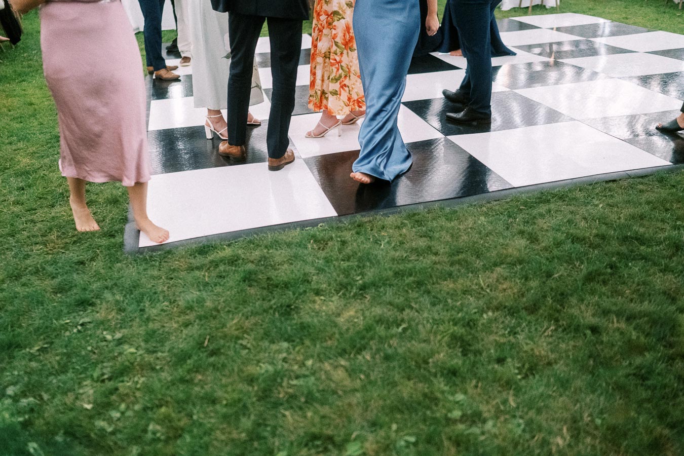 Wedding guests dancing on a black and white checkered floor on grass during an outdoor tented reception near Chatham-Kent, Ontario, Canada.
