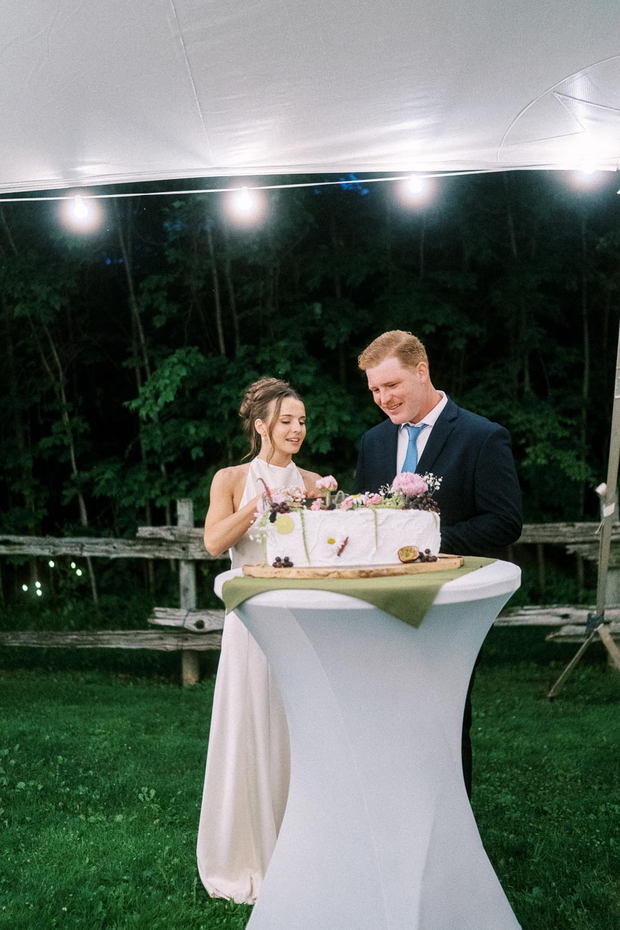 Bride and groom cut a decorated wedding cake under a lit white tent at a private farm estate near Chatham-Kent, Ontario.