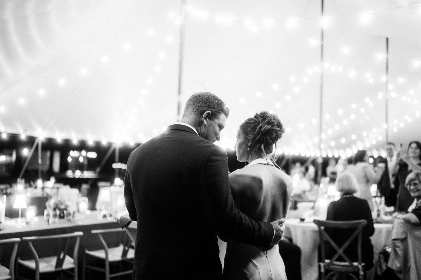 Black and white photo of a couple embracing during a tented outdoor wedding reception near Chatham-Kent, Ontario.