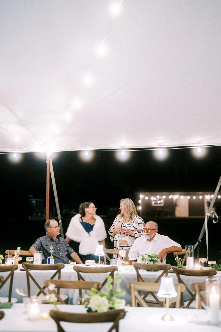Guests at an outdoor tented wedding dinner on a private farm estate near Chatham-Kent, Ontario, with string lights, candles, and rustic tables.