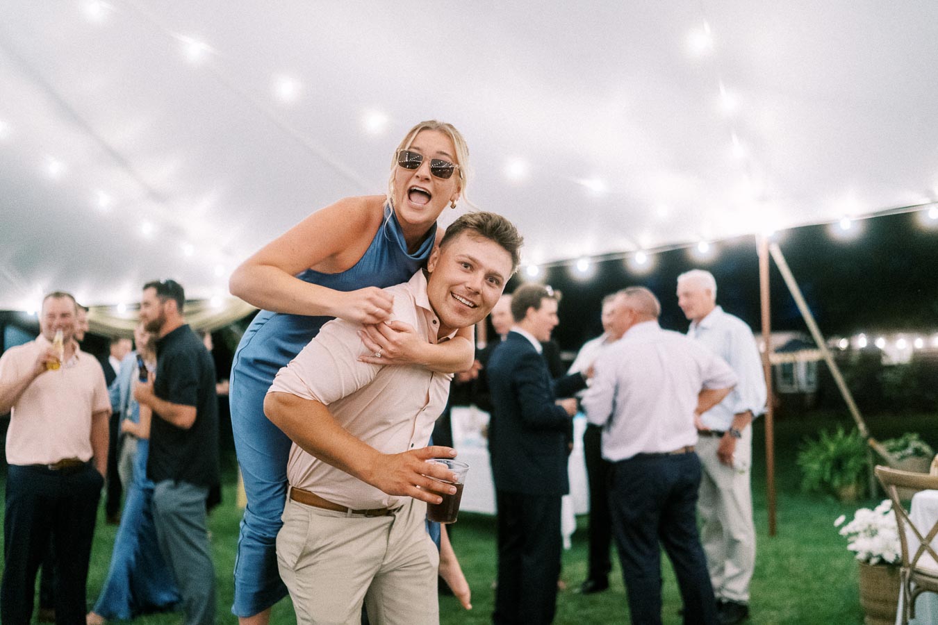 Wedding guests laughing under a lit reception tent during an outdoor private estate celebration near Chatham-Kent, Ontario, Canada.