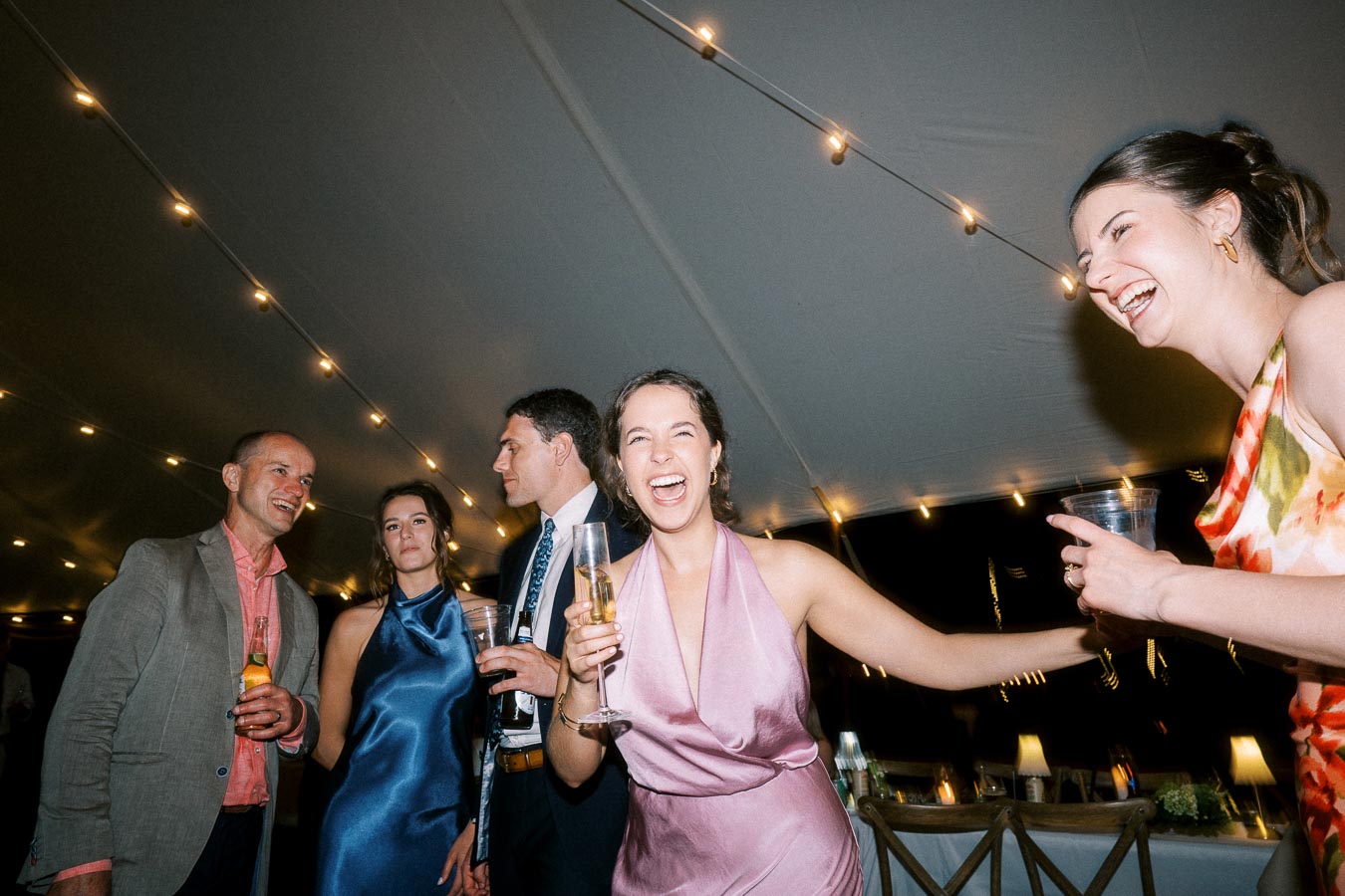 Guests laughing and holding drinks under string lights inside a wedding tent near Chatham-Kent, Ontario, Canada.