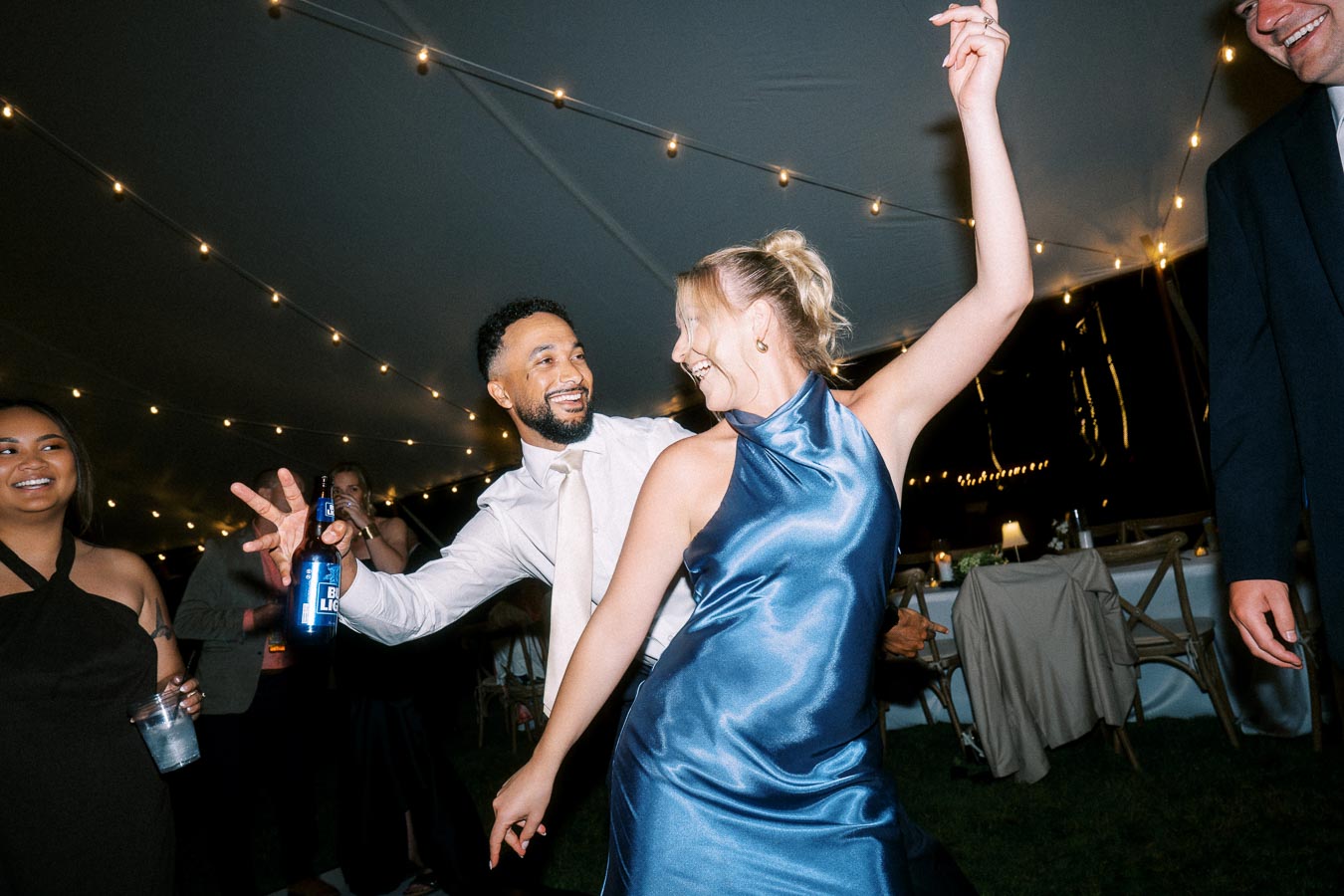 Wedding guests dancing under string lights inside a tent at an outdoor private estate wedding near Chatham-Kent, Ontario, Canada.