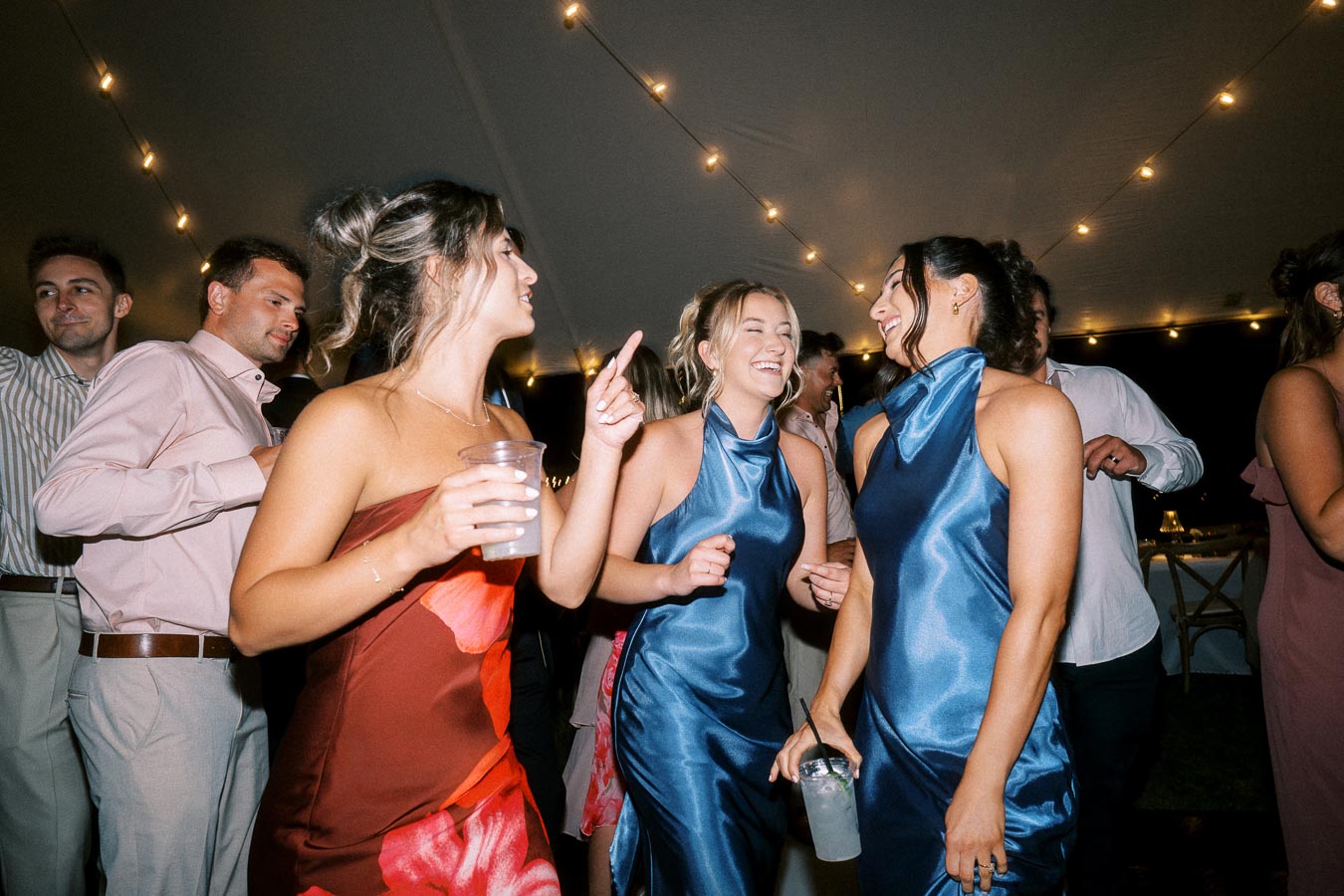 Wedding guests dancing inside a tent with string lights at an outdoor farm wedding near Chatham-Kent, Ontario, Canada.