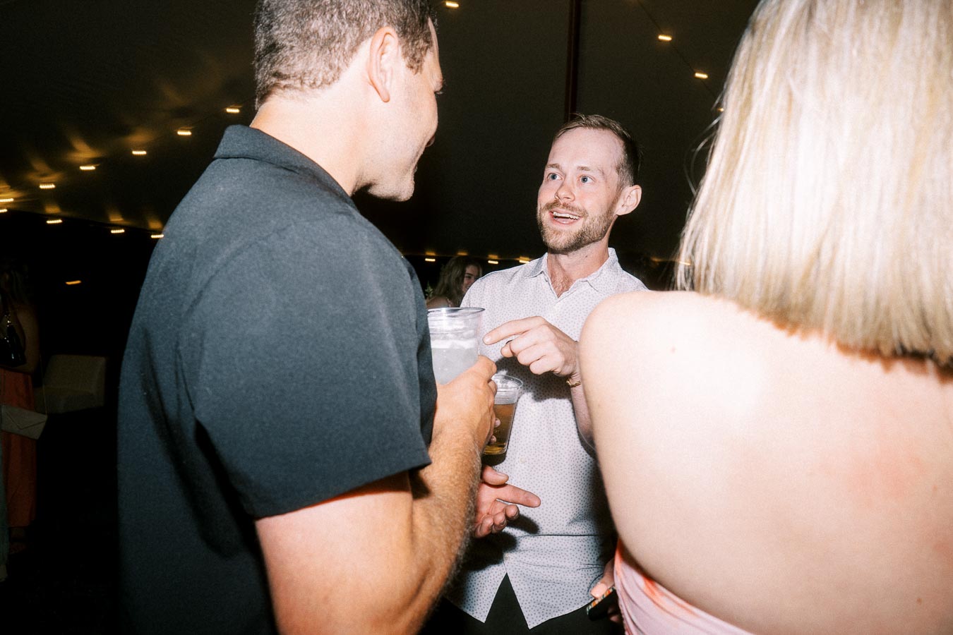 Wedding guests talking and drinking inside a lit reception tent near Chatham-Kent, Ontario, Canada.