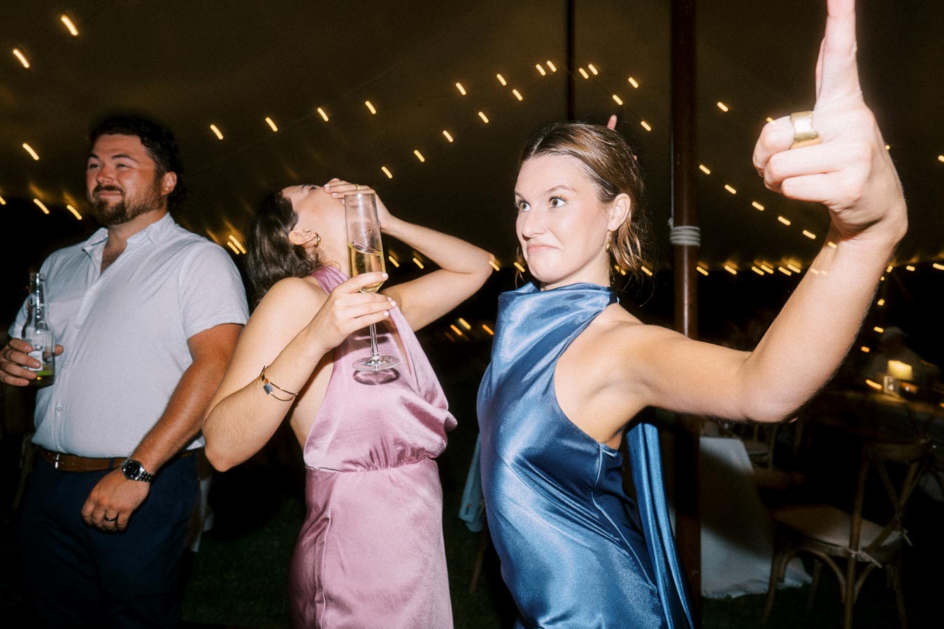 Wedding guests dancing and drinking under a tent with string lights at a private farm estate near Chatham-Kent, Ontario, Canada.