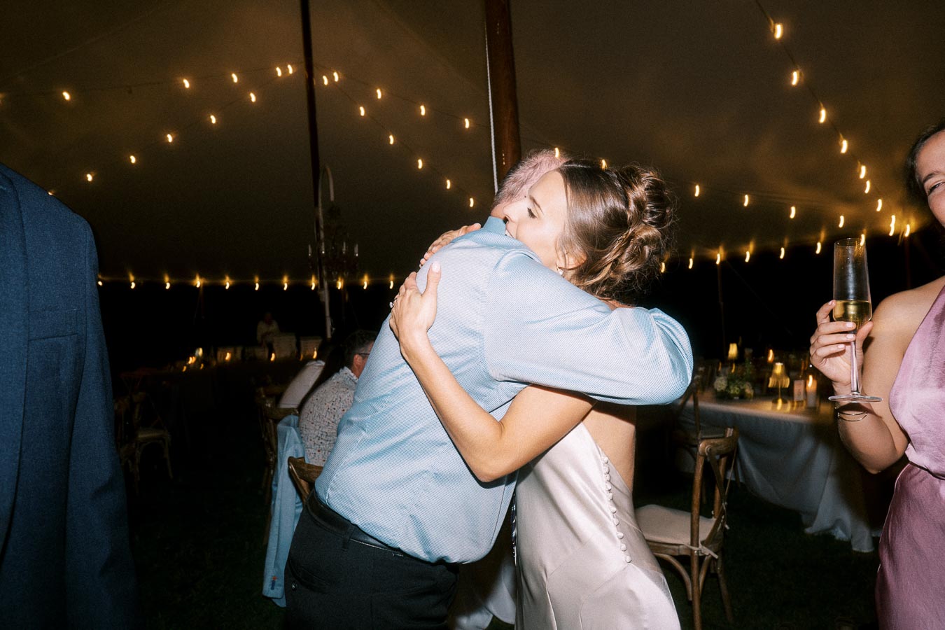 Bride hugging a guest during a night wedding reception inside a lighted tent on a private farm estate near Chatham-Kent, Ontario, Canada.