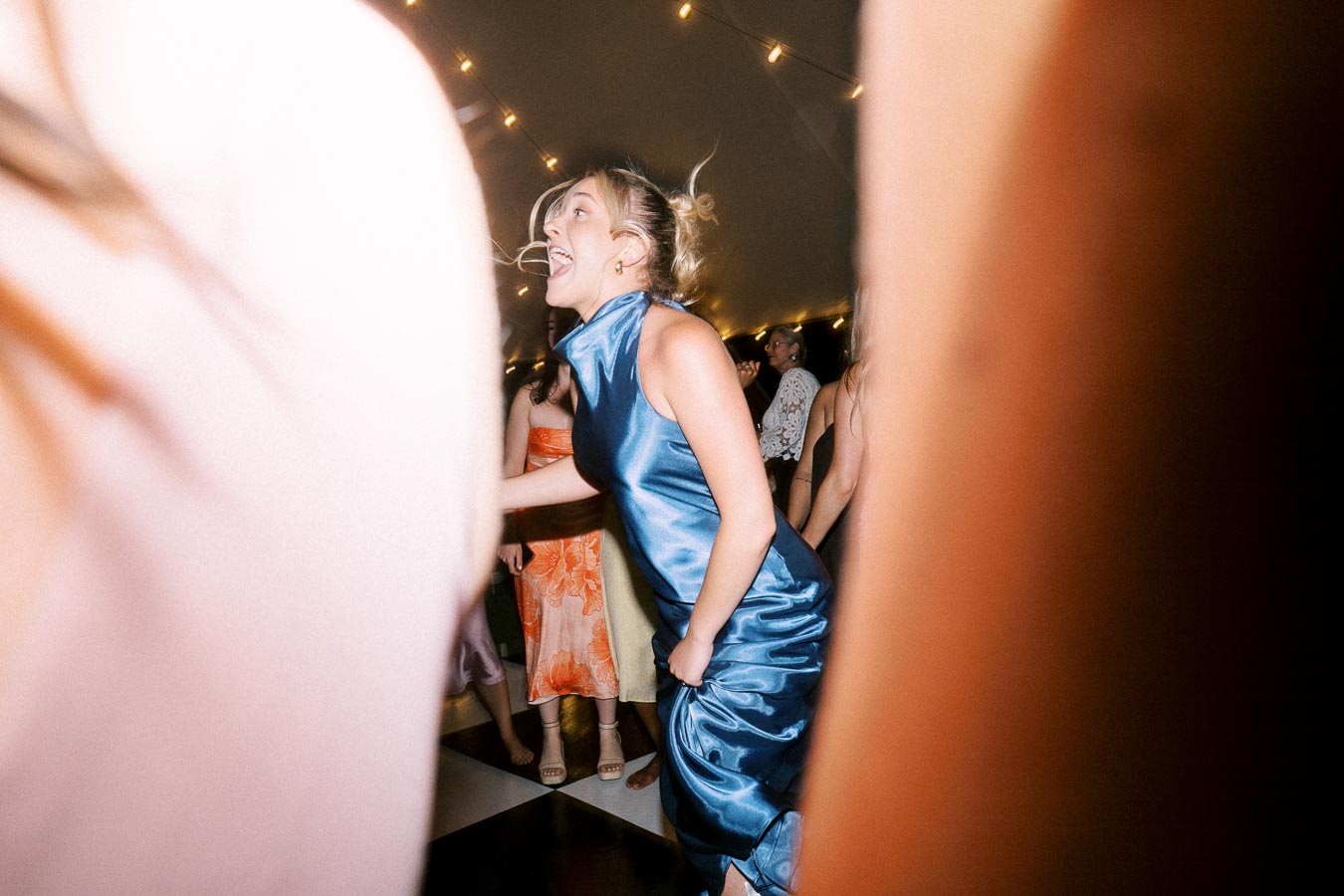 Wedding guest dancing in a blue satin dress under string lights inside a tent near Chatham-Kent, Ontario.