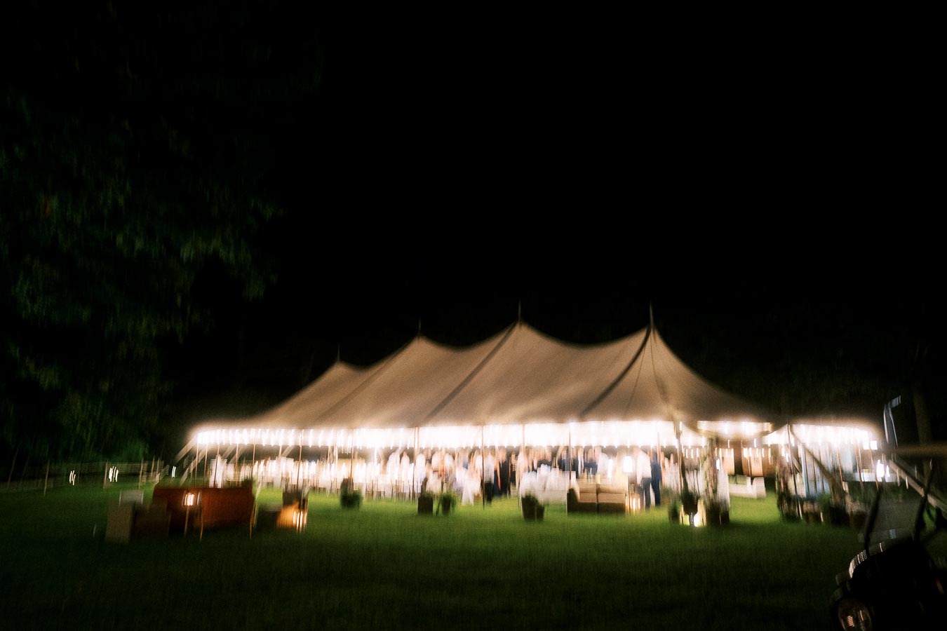 Outdoor tented wedding reception at night on a private farm estate near Chatham-Kent, Ontario, with glowing lights and guests inside a large marquee.