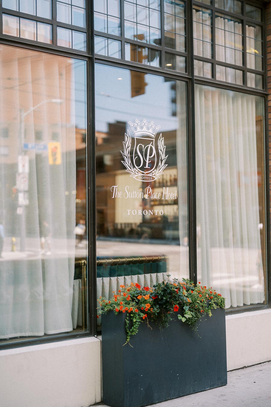 Sutton Place Hotel Toronto window with logo, curtains, and orange flowers in planter