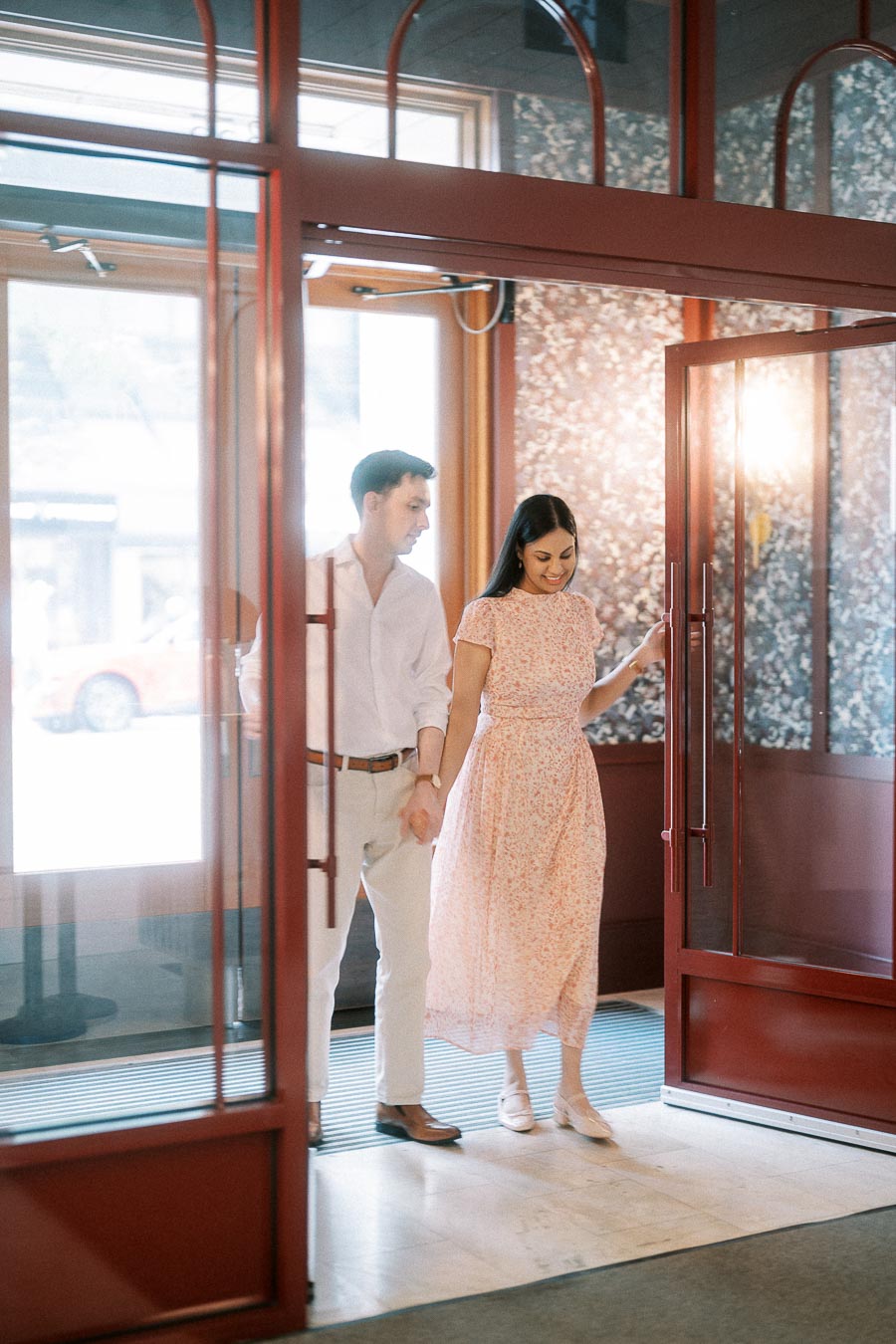 Couple holding hands while entering through red glass doors in Toronto