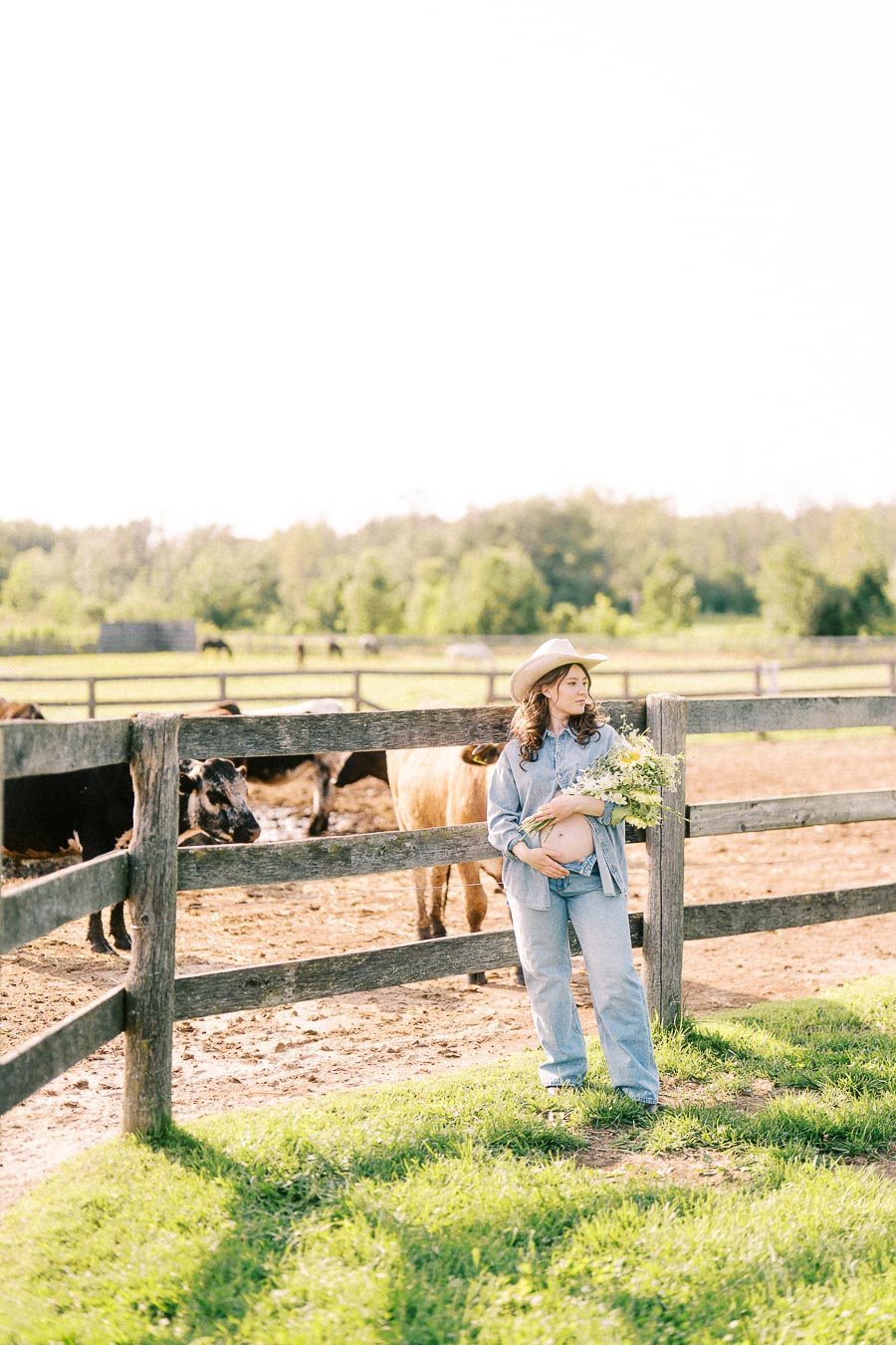 Pregnant woman in a cowboy hat standing by a cattle fence at The Green Acres