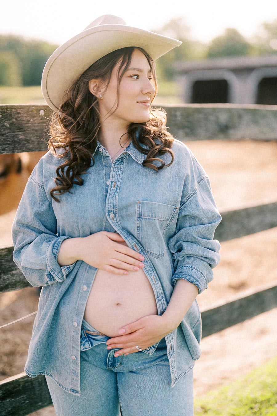 Pregnant woman in cowboy hat posing by a farm fence at The Green Acres