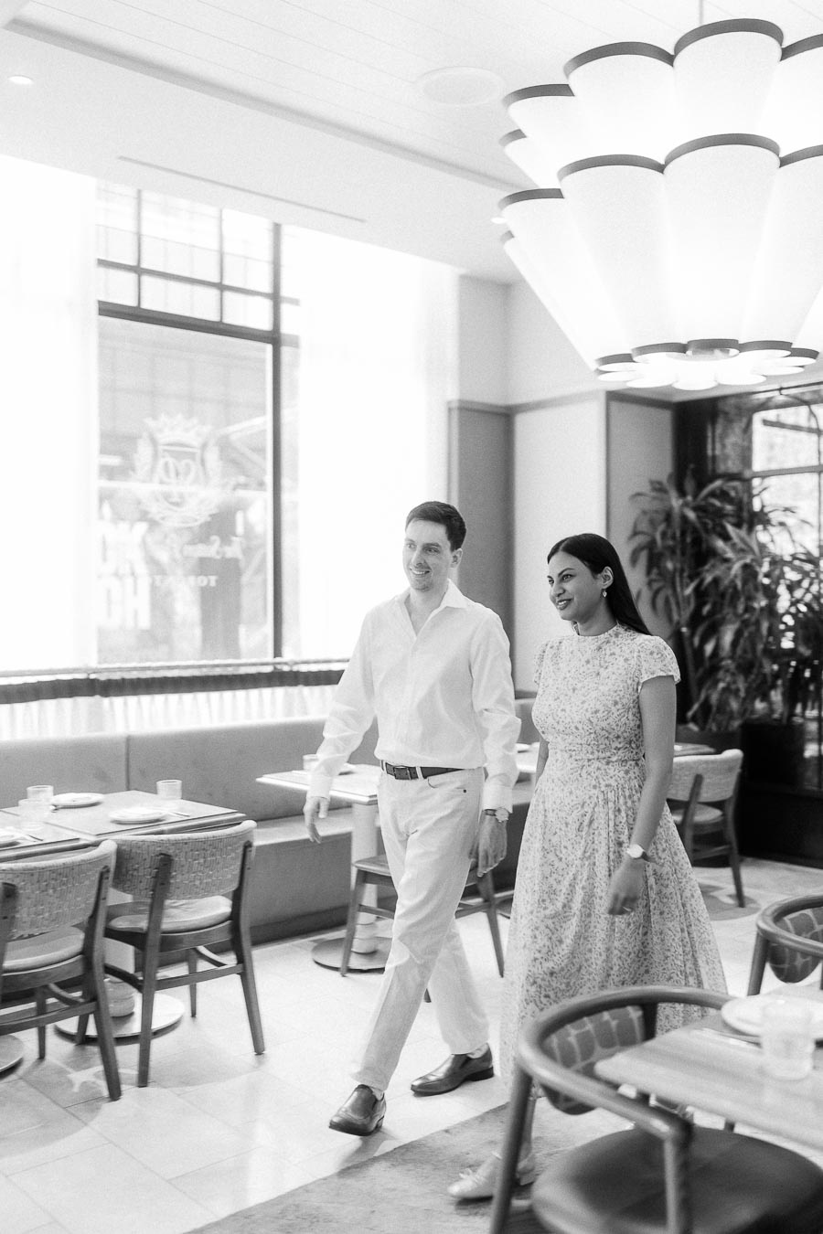 Couple walking through a bright Toronto restaurant dining room beneath a sculptural chandelier