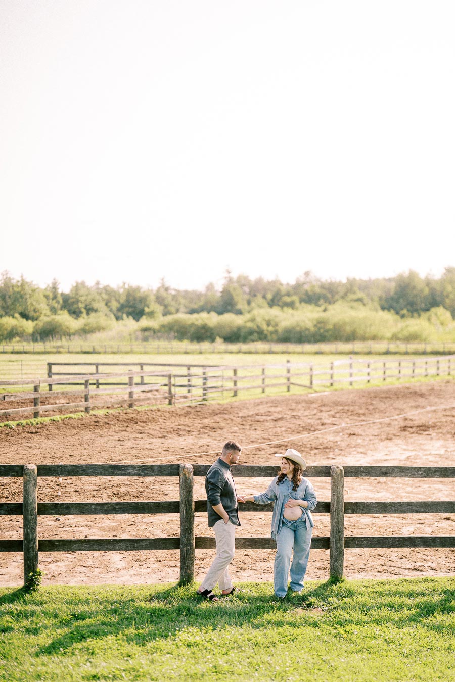 Expectant couple standing by a wooden paddock fence at The Green Acres