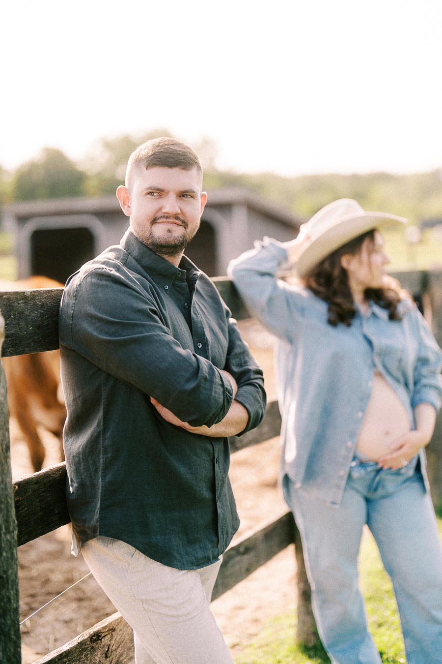 Expectant couple by a farm fence with horses in Flamborough, Ontario