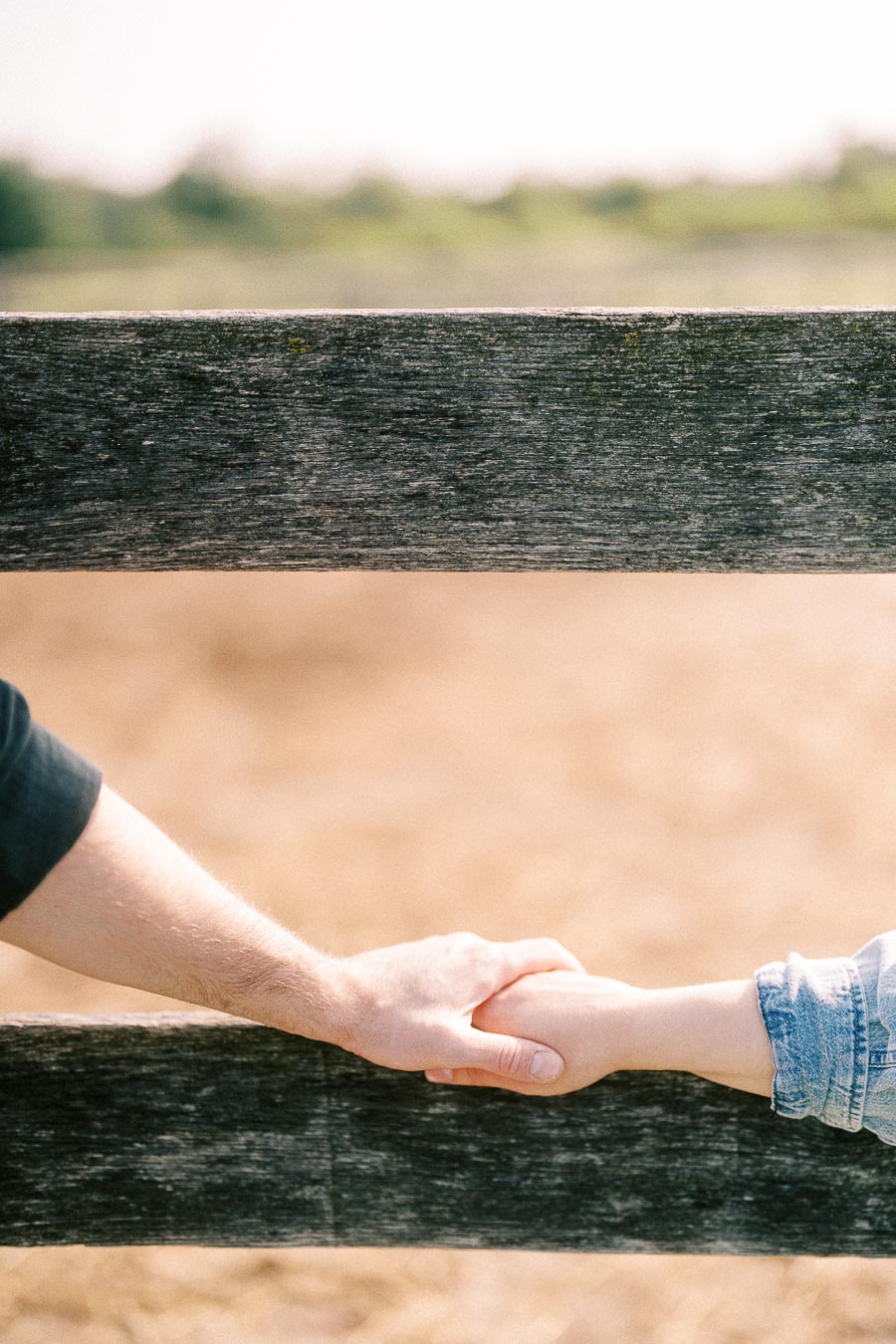 Couple holding hands through a weathered wooden fence at The Green Acres