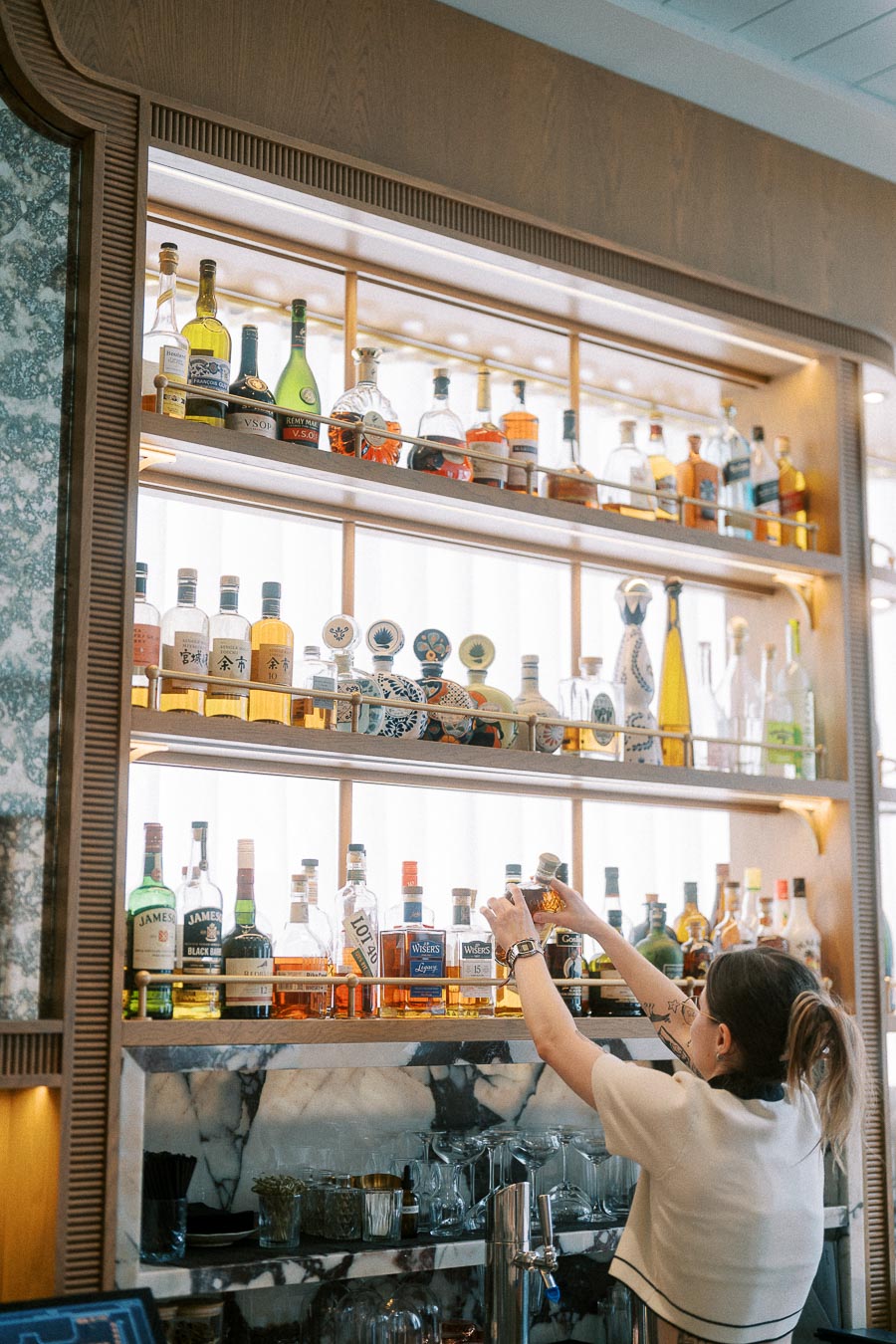 Bartender reaching for bottles on a backlit bar shelf in Toronto