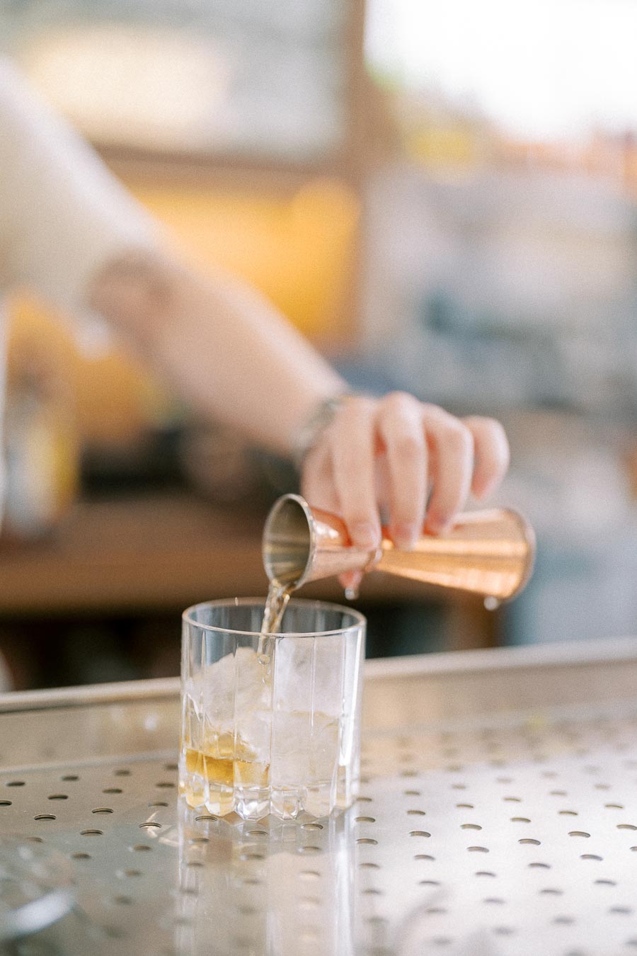 Hand pouring cocktail from a copper jigger into a rocks glass with ice