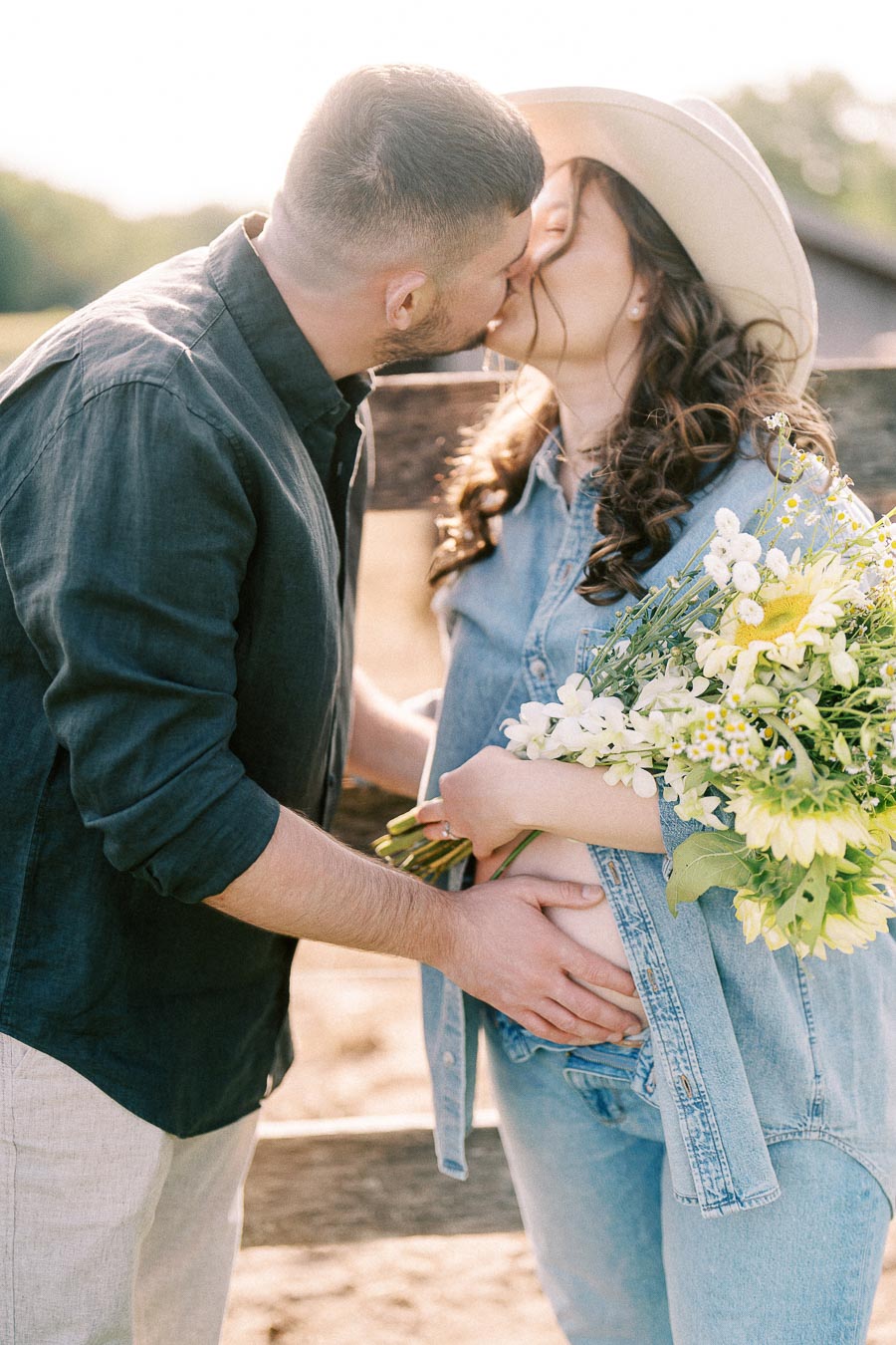 Expectant couple kissing as she holds flowers at The Green Acres