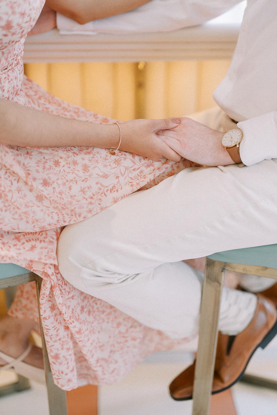 Couple holding hands while seated, with floral dress and white suit details