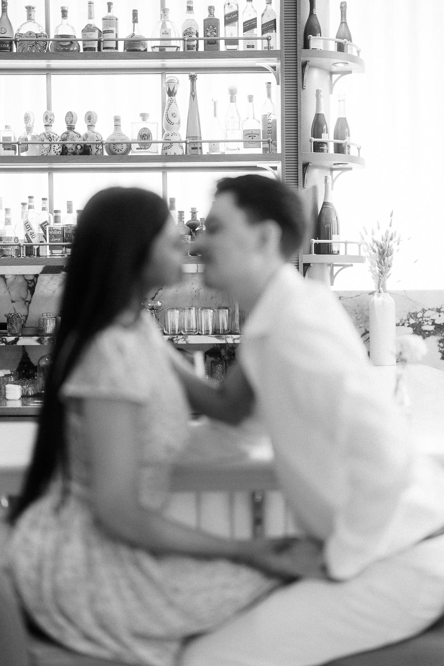 Blurred couple sitting close in a bright Toronto bar with liquor shelves behind them