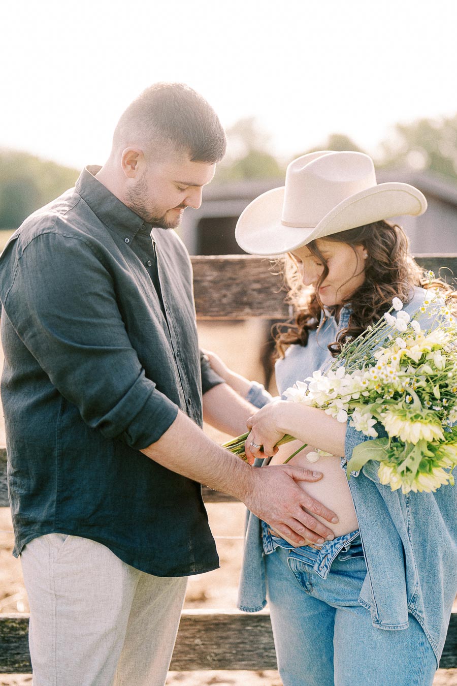 Expectant couple with bouquet by wooden fence at The Green Acres