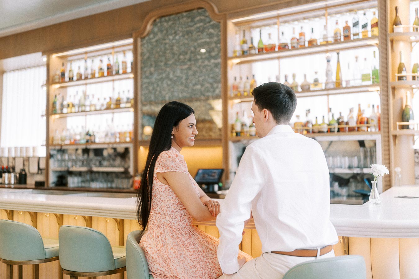 Couple smiling at a bright hotel bar with illuminated bottles behind them