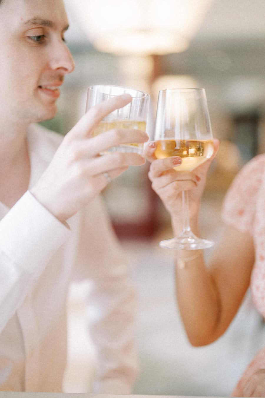 Couple clinking wine and cocktail glasses during a soft indoor engagement session