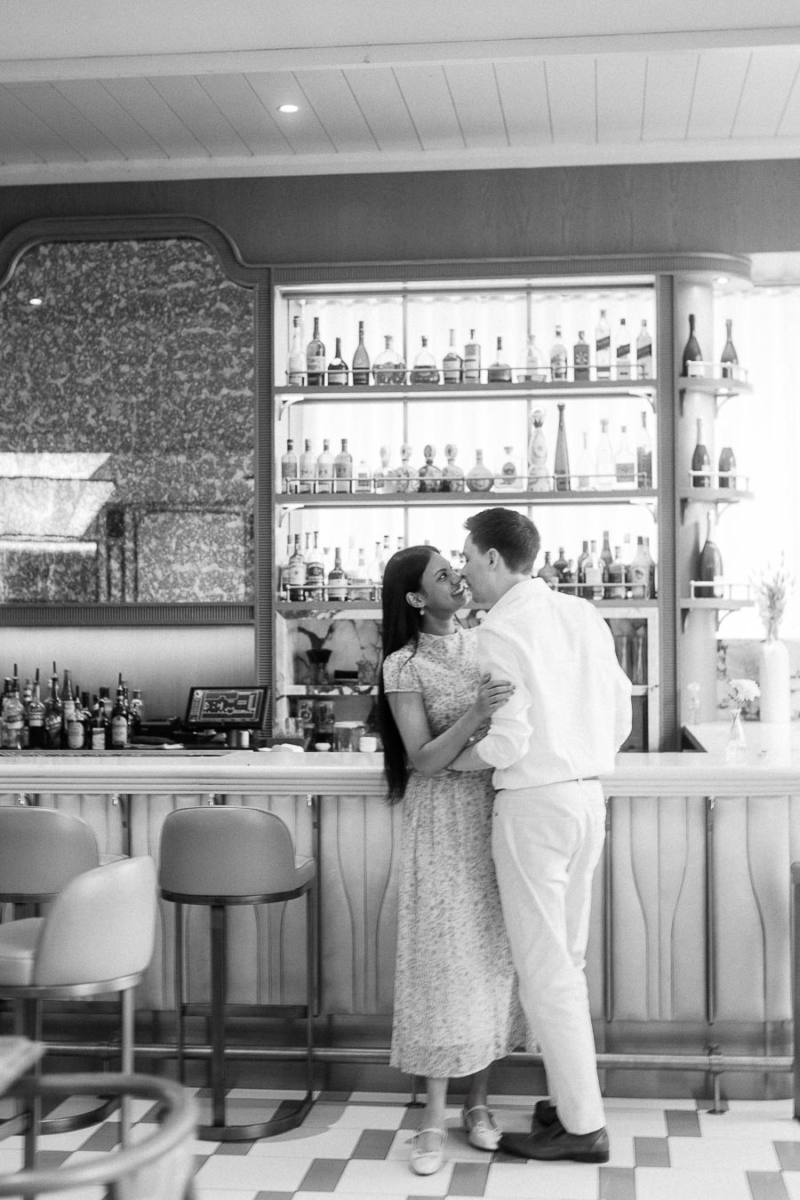 Couple embracing at a bar with backlit shelves of bottles
