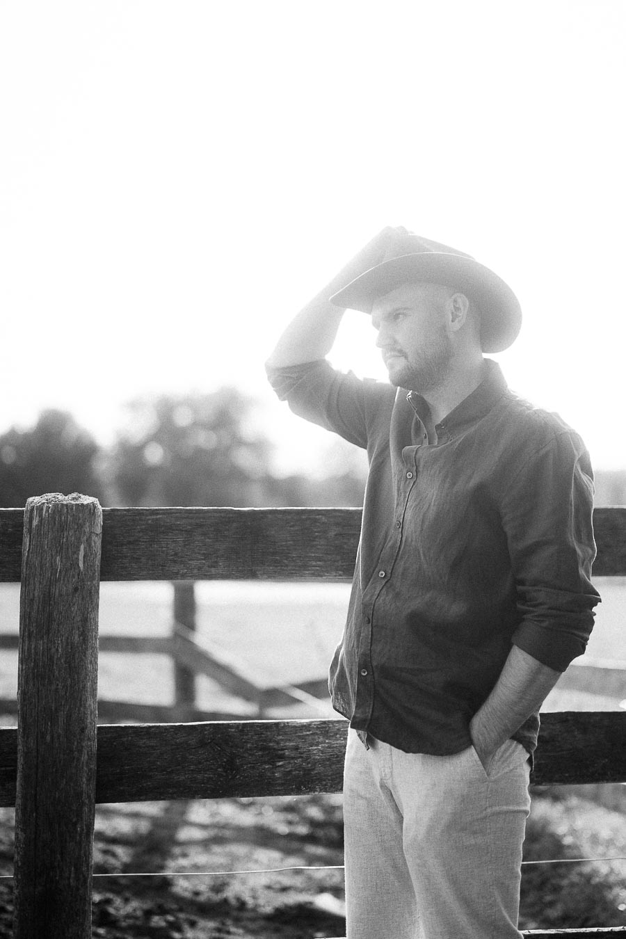 Man in cowboy hat standing by a wooden fence in black and white