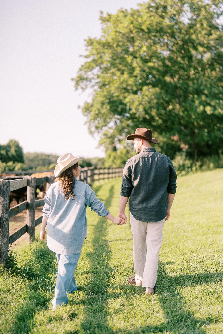 Expectant couple holding hands along a farm fence at The Green Acres