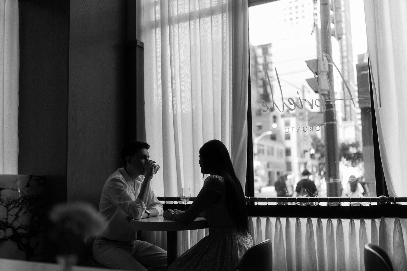 Couple seated by a restaurant window with sheer curtains in Toronto