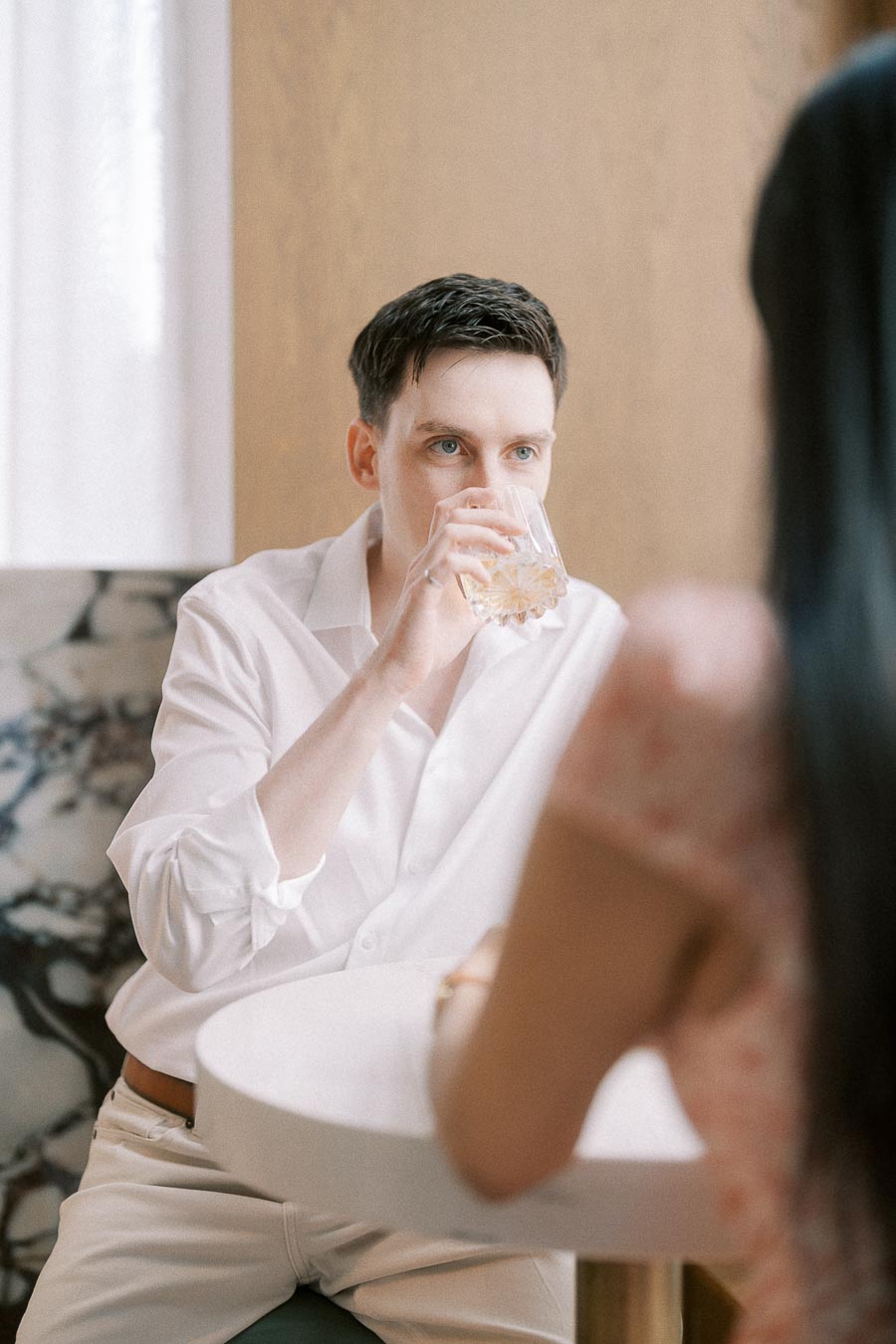 Man in a white shirt sipping a drink across from his partner at a café table