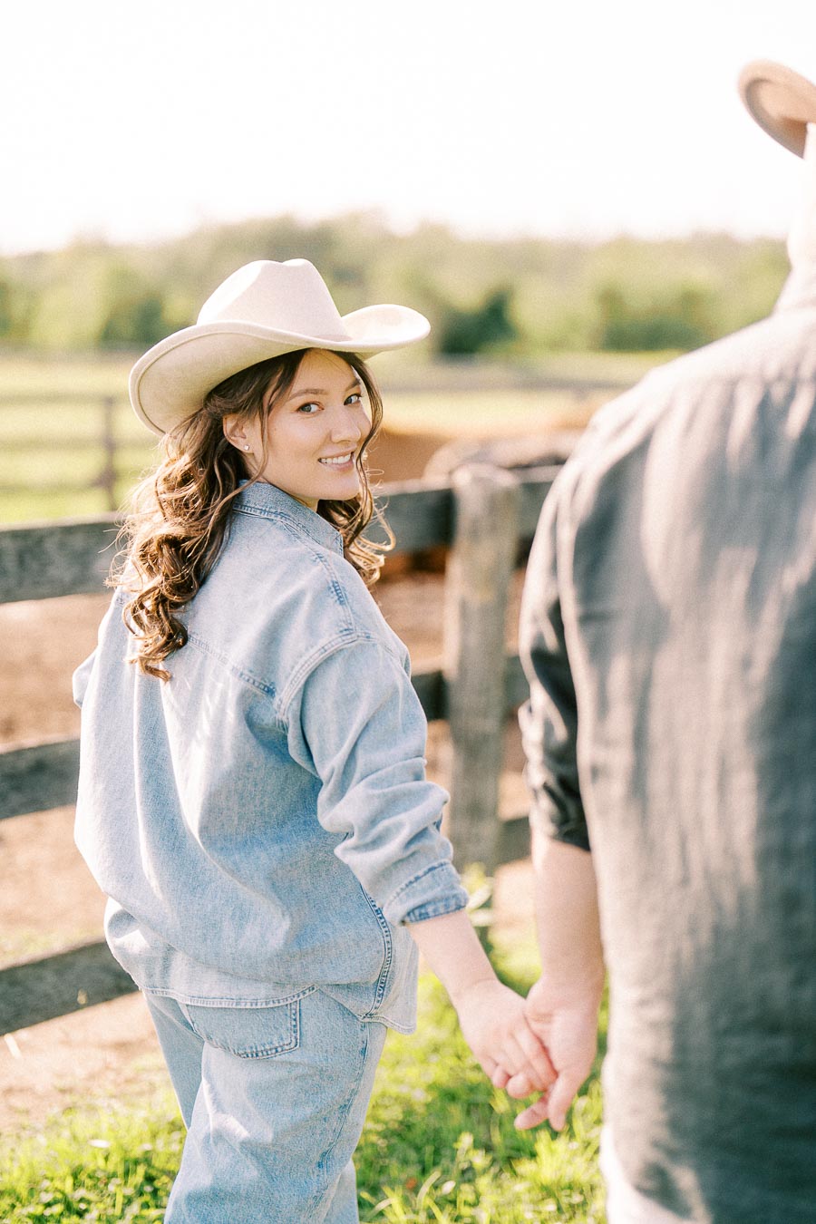 Pregnant woman in cowboy hat holding hands by a farm fence in Flamborough