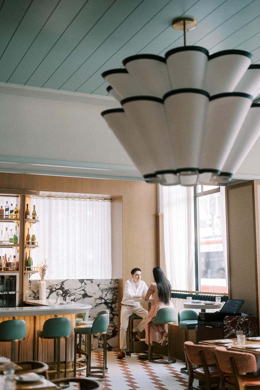 Couple seated at a stylish bar beneath a large chandelier in Toronto